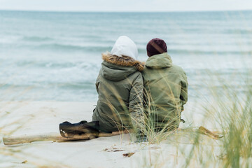 A couple in love sits on the beach, dreams and looks at the sea. Rear view, against the backdrop of...