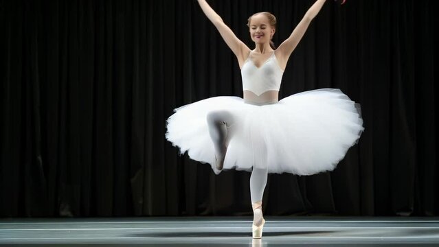 A ballerina in a white tutu gracefully extends her leg and arm, her body forming a perfect line against a dark background. The image captures the elegance, strength, and dedication of ballet.
