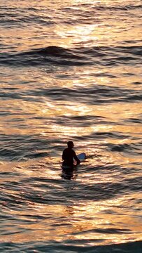 Slow motion vertical drone footage of a surfer sitting on his surfboard at Tamarama Beach, Australia