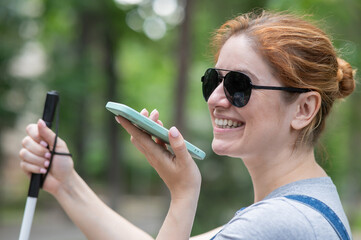 Happy blind woman sitting on bench and talking on smartphone. 