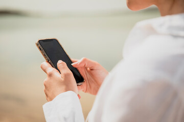 Close-up of a girl's hands typing on her smartphone next to a lake