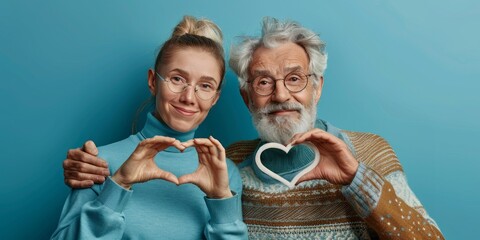 Happy senior couple in sweater showing heart symbol with hands over pastel blue background.