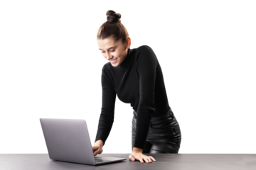 A smiling woman standing at a table with a laptop, isolated on a white background, depicting a modern professional or businesswoman