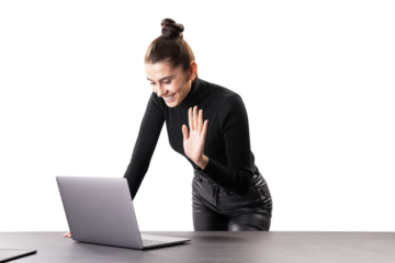 A smiling woman standing at a table with a laptop, waving in greeting, on a white background, concept of virtual online meetings