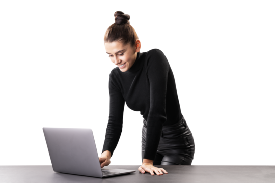 A smiling woman standing at a table with a laptop, isolated on a white background, depicting a modern professional or businesswoman