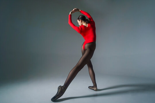 young ballerina in a red bodysuit and pointe shoes poses for ballet elements in a photo studio
