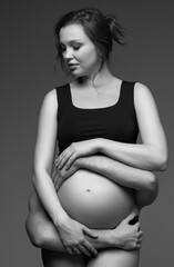 Black and white photo of man behind female and hugs her pregnant exposed belly. - 783563098