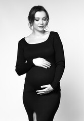 Black and white portrait of pregnant female in black dress with hands near pregnant belly. - 783563099