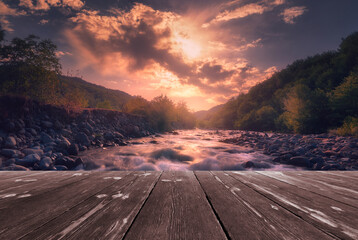 Magical sunrise over fast flowing mountain river with empty wooden batten bridge. Natural template landscape