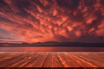 Fototapeta na wymiar After the storm. Beautiful red clouds over the lake after rain with empty wooden table. Natural template landscape
