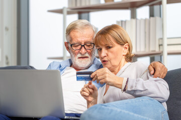 Senior couple with laptop shopping online at home and paying with credit card