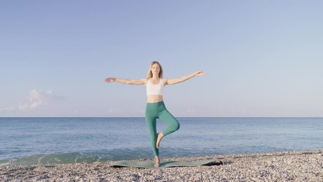 Young woman is doing yoga on the beach near the sea. A girl t does yoga exercises, and against the backdrop of the sea surf and a beautiful sky