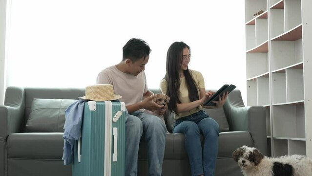 Asian couple packing clothes for a trip abroad together in the bedroom, man and woman sitting on the floor in the living room near suitcases with belongings going on vacation