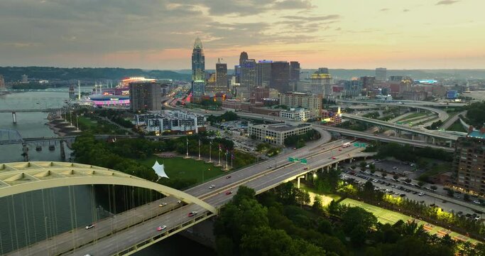 Downtown district of Cincinnati city in Ohio, USA at sunset with driving cars traffic on Daniel Carter Beard Bridge and brightly illuminated high skyscraper buildings. American travel destination