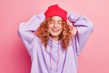 Smiling Young Woman in Red Beanie and Purple Hoodie Against Pink Background