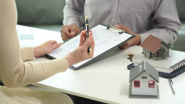 A sales representative offers a home purchase contract to purchase a house or apartment. or talk about loans interest rate and insurance Client and real estate agent shaking hands in office 4k