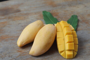 Ripe yellow mango fruit with mango sliced and leaves on wood background