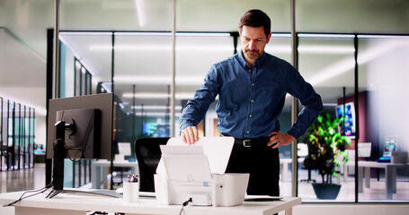 Irritated Businessman Looking At Paper Stuck In Printer