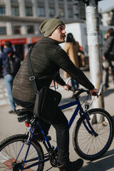 A man in winter clothes pauses on his bike in an urban setting, looking back as people walk by.
