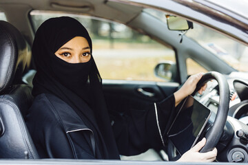 Middle Eastern Woman Driving a Car face covered black niqab dressing , Looking at Camera