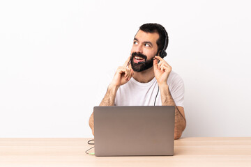Telemarketer caucasian man working with a headset and with laptop thinking an idea while looking up.