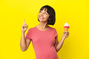 Pregnant woman holding a cornet ice cream isolated on yellow background pointing up a great idea