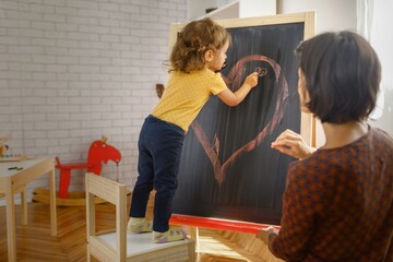 Child drawing heart on chalkboard at home. Mother and daughter drawing at home. 