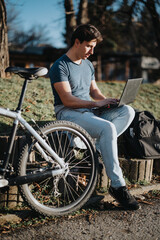 Obraz premium A man enjoys a sunny day in the park, sitting with his laptop next to his bicycle, embodying a blend of work and leisure.