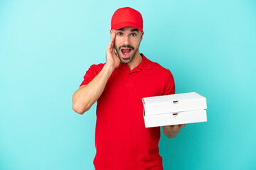 Delivery caucasian man picking up pizza boxes isolated on blue background with surprise and shocked...