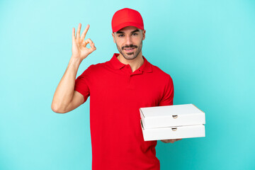 Delivery caucasian man picking up pizza boxes isolated on blue background showing ok sign with...
