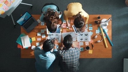Top down aerial view of skilled designer hold logo while discuss with team. Aerial business group...