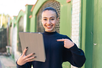 Young moroccan girl holding a tablet at outdoors with surprise facial expression