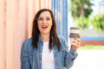 Middle aged woman holding a take away coffee at outdoors with surprise and shocked facial expression