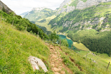 Fototapeta na wymiar View from the walking trail from Altenalp towards Aescher mountain hut, iron closed fence preventing cattle to pass. Below in the valley the beautiful Seealpsee lake surrounded by Swiss mountains.