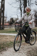 A mature female retiree smiles while riding her bicycle through a tranquil park setting.