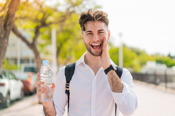 Young handsome man with a bottle of water at outdoors shouting with mouth wide open