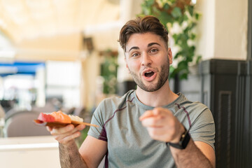 Young handsome man holding sashimi at outdoors surprised and pointing front