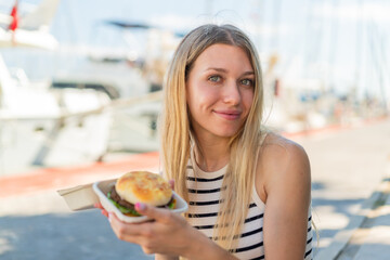 Young blonde woman at outdoors holding a burger