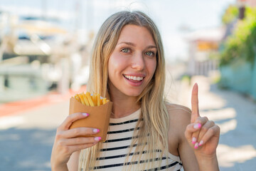 Young blonde woman holding fried chips at outdoors pointing up a great idea