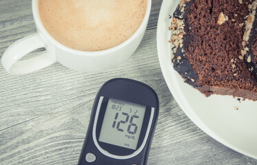 Glucose meter with high result sugar level, sweet chocolate cake and cup of coffee with milk. Nutrition during diabetes