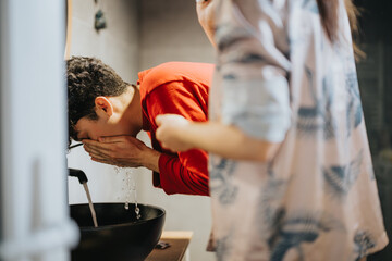 A person is washing their face, splashing water from a sleek bathroom basin, depicting morning...