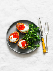 Delicious tapas, appetizer - grilled potatoes with sour cream and red caviar and arugula salad on a light background, top view