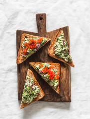 Delicious tapas, appetizer, snack - bruschetta with avocado, eggs, gherkins, greens spread and red caviar on a wooden chopping board on a light background - 783616230