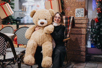 Happy woman embracing large teddy bear in christmas decorated cafe.