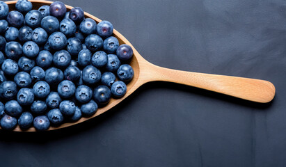 Juicy ripe blueberries in a paddle cutting board on dark surface. - obrazy, fototapety, plakaty