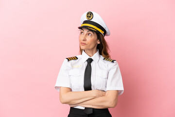 Airplane middle aged pilot woman isolated on pink background looking up while smiling
