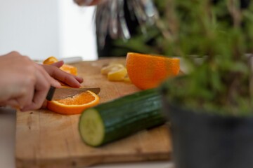 Closeup of a chef cutting orange and cucumber on a cutting board in the kitchen