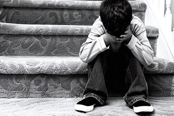 Upset child sitting on stairs with head in hands. Monochrome image capturing childhood sadness. Design for poster, child psychology and parenting materials