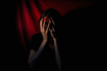 Person in despair with hands on face in dark, theatrical setting. Emotional pain and drama concept. Design for theatrical posters and mental health awareness.