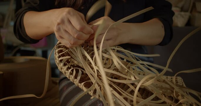 An Asian female artisan who is a rural villager weaving folk baskets made from leftover paper band to sell as extra income in the community shop.